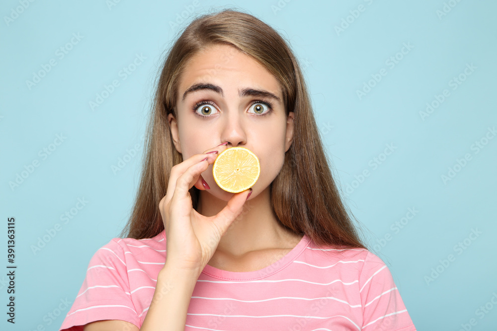Young girl holding piece of lemon on blue background Young girl holding piece of lemon on blue background
