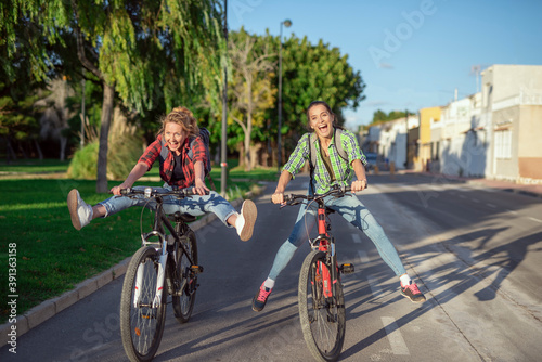 Two pretty young caucasian girls having fun on bicycles along the street. Best friends enjoying a day on bikes. Sunny summer evening