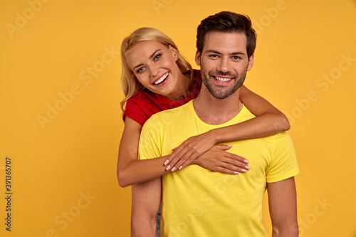 Smiling young couple friends in colored t-shirts posing isolated on yellow wall background studio portrait. People emotions lifestyle concept. Mock up copy space. Hugging
