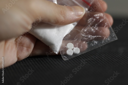 The hand of a drug addict, holding tightly clear bags with powdered cocaine to snort and contraband pills inside.