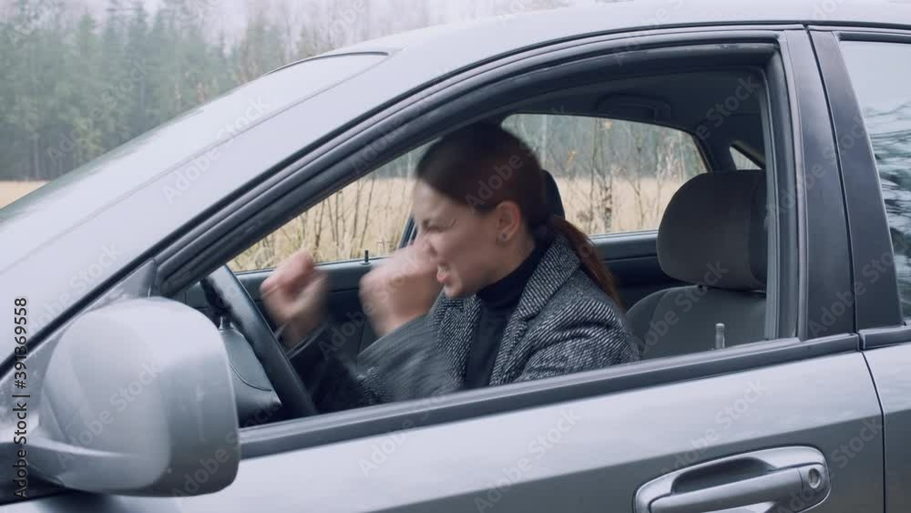 Aggressive young woman driver is stuck in the car hitting leaning on steering wheel taking a breath. Car problem.