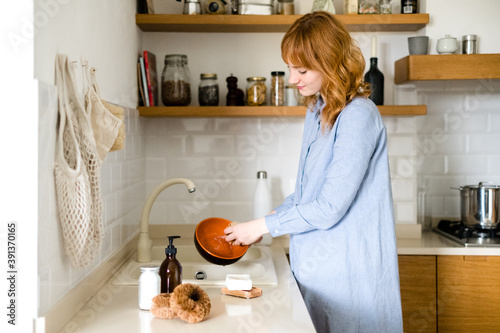 Young Woman in the kitchen washing dishes with natural and zero waste products