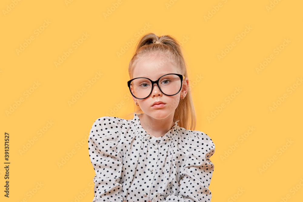 Portrait of a blonde Girl child with glasses for vision looking at the camera. Black-rimmed glasses. Yellow isolated background.