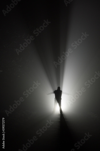Silhouette of a man, in the rays of light at foggy night