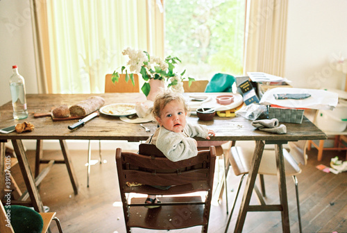 Little baby girl sitting in a highchair in a messy kitchen