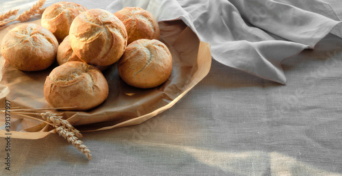 Kaiser or Vienna rolls on baking paper. Table covered with beige linen tablecloth. photo