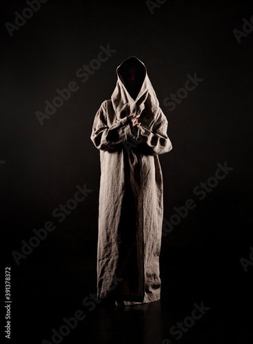 A young woman in a raincoat of coarse cloth on her naked body is isolated on a black background.