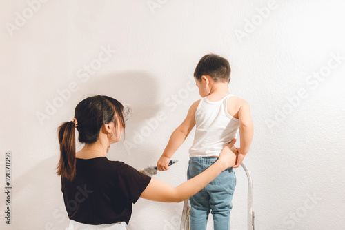 Young mother teaching son to paint the wall. Mom and child moment. photo