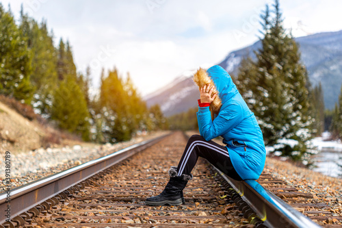 Pretty young traveler woman sitting on railroad, full of thoughts. Adventure in the Canadian mountains. Concept about travel, lifestyle, holiday and environment. 