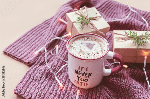 A cup of hot drink with foam and two boxes of gifts on a knitted sweater, decorated with a garland