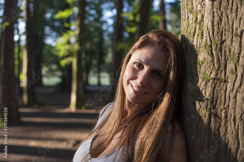 Lindo retrato de mulher encostada em uma árvore com a luz do Sol iluminando seu rosto photo