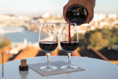 Pouring of fortified dessert ruby  tawny port wines in glasses with view on Douro river  porto lodges of Vila Nova de Gaia and city of Porto  Portugal