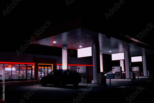 Valokuva A gas hose is installed in a car at a night gas station with a store in the background and bright lights