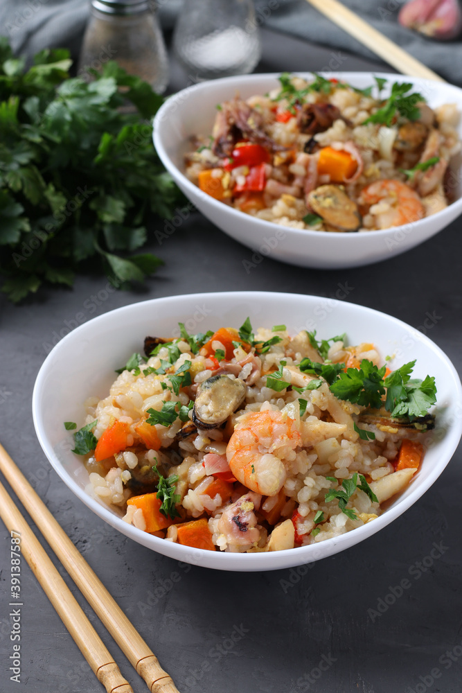 Two plates fried rice with seafood, vegetables, ginger and parsley on dark background. Asian cuisine. Vegetarian food. Vertical format. Closeup
