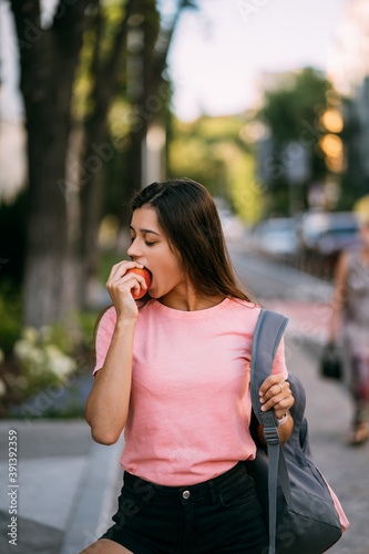 Young woman biting apple against a street background