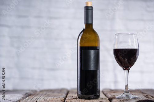 Bottle and glass with red wine on rustic wooden table on white brick background. Concept of alcoholic drink. Photo for advertising and product promotion. Space for text.