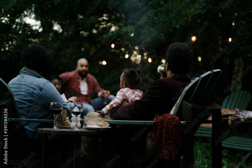 Friends gathered for evening party in backyard around firepit Friends gathered for evening party in backyard around firepit