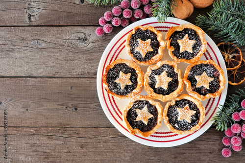 Plate of Christmas mincemeat tarts. Top down view table scene over a dark wood background.