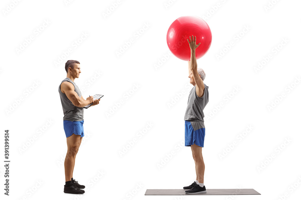 Full length profile shot of an elderly man exercising with a fitness ball with a personal fitness instructor Full length profile shot of an elderly man exercising with a fitness ball with a personal fitness instructor