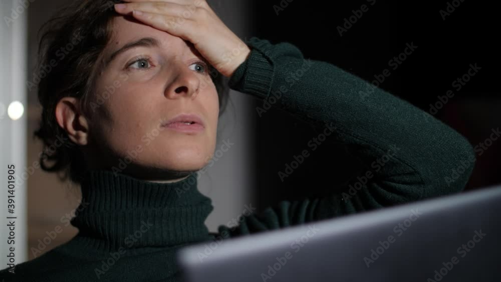 Frustrated and angry young woman working with laptop at night. Stylish millennial girl writing on computer, thinking, touching forehead and looking into distance. Dark background at home. Frustrated and angry young woman working with laptop at night. Stylish millennial girl writing on computer, thinking, touching forehead and looking into distance. Dark background at home.