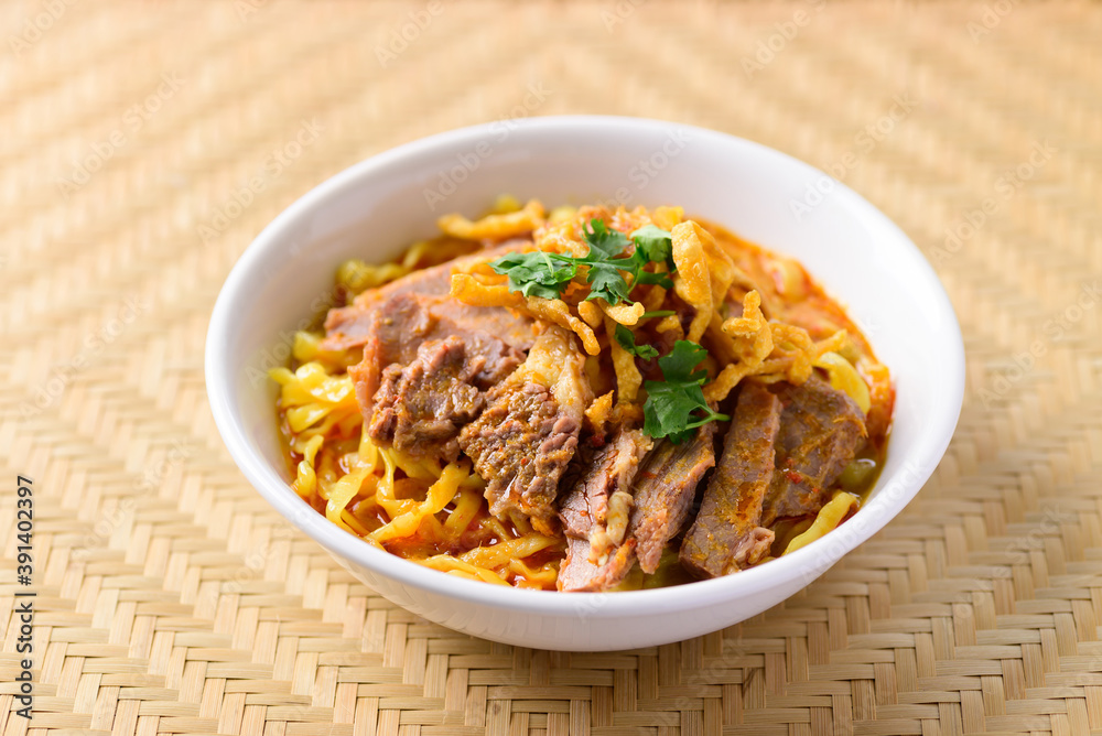 Northern Thai food (Khao Soi), Spicy curry noodles soup with beef in a bowl on woven bamboo sheet Northern Thai food (Khao Soi), Spicy curry noodles soup with beef in a bowl on woven bamboo sheet