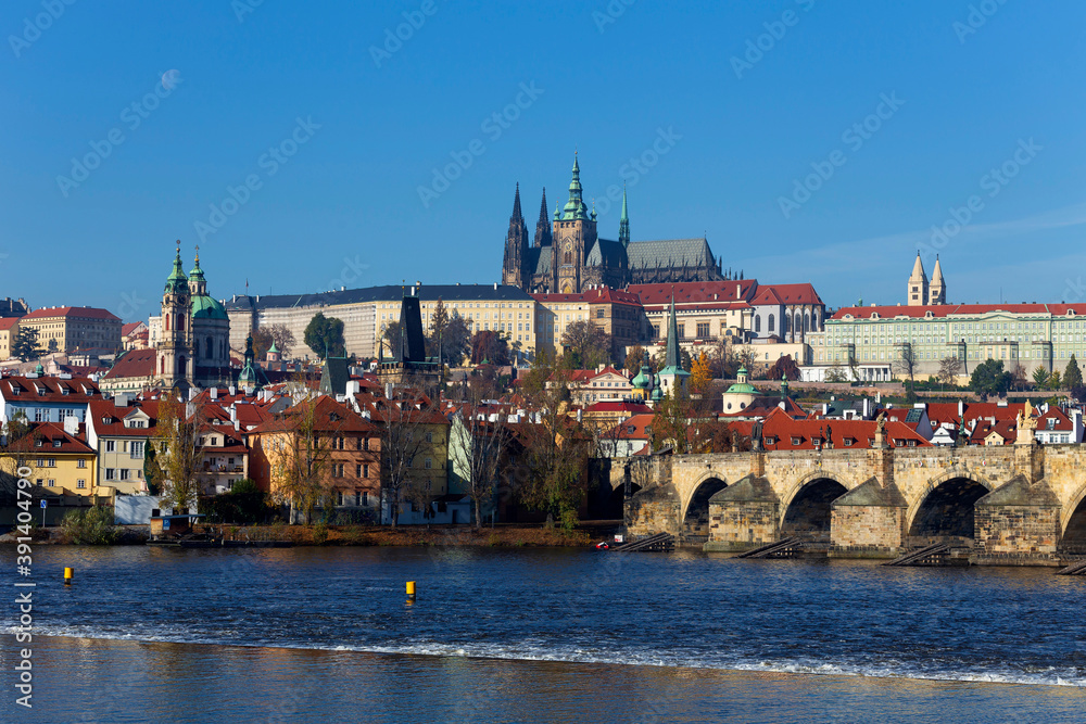 Obraz premium Autumn colorful Prague Lesser Town with gothic Castle and Charles Bridge above River Vltava in the sunny Day, Czech Republic