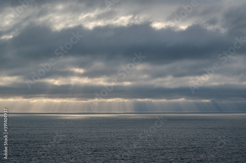 Sun rays coming down from the clouds over the ocean. View of the horizon line on a cloudy sunset