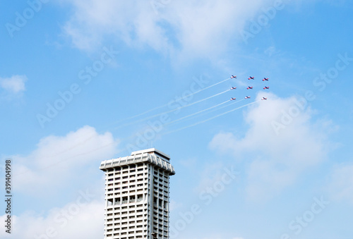 Photography A squadron of aircraft performing an airshow with beautiful formation passing by tall building on a beautiful day with blue sky and white clouds