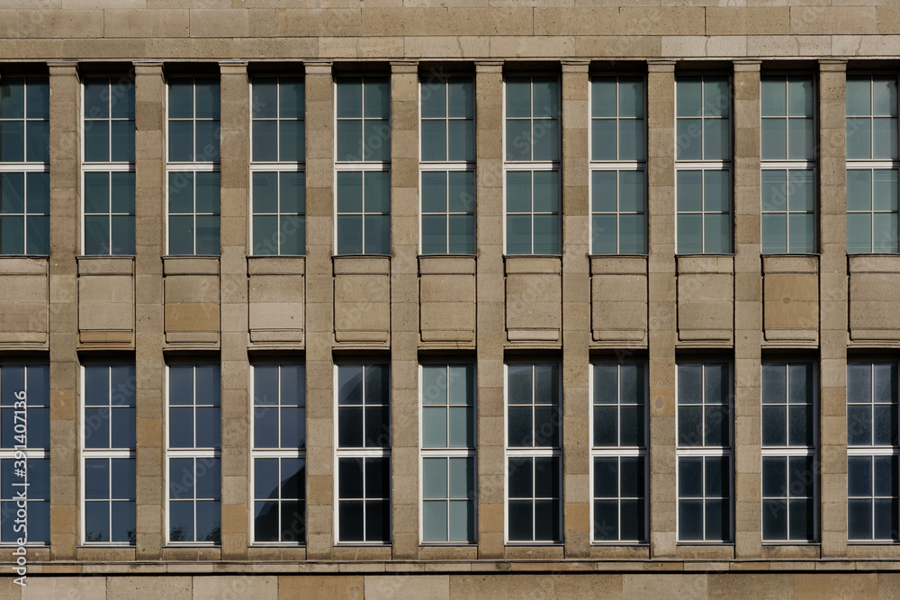 Front exterior view of modern facade with cream brown rough granite stone tile wall and high windows on symmetric rectangular pattern. Front exterior view of modern facade with cream brown rough granite stone tile wall and high windows on symmetric rectangular pattern.