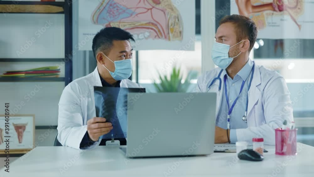 Multi-race young doctor couple negotiating in medical office. Chief asian therapist talking to assistant discussing lung disease xray image coronavirus infection. Multi-race young doctor couple negotiating in medical office. Chief asian therapist talking to assistant discussing lung disease xray image coronavirus infection.