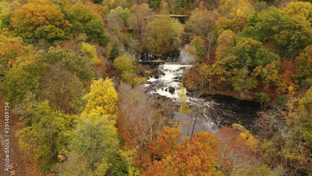 An aerial shot of the colorful fall foliage in upstate NY. The camera dolly out from a waterfall & over the autumn landscape. Then old train tracks come into view on this bleak & cloudy day.