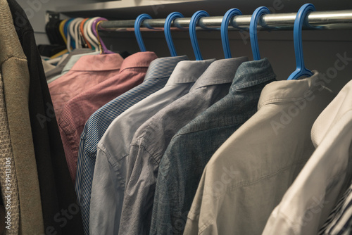 clothing on hangers in a walk-in closet with organized mens dress shirts 