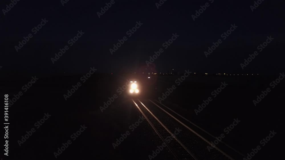 Freight train lights prairie railroad tracks on dark purple night