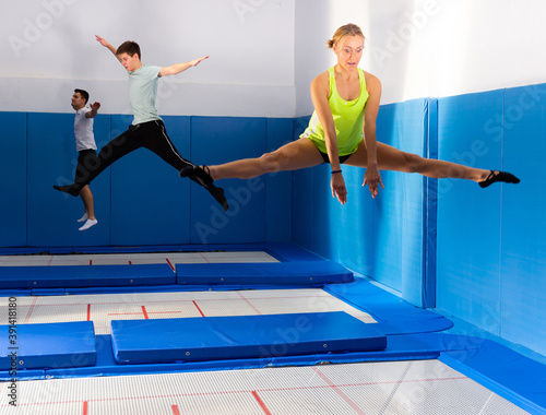 Smiling female and males jumping and bouncing on a trampoline during workout in modern fitness center