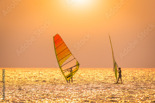 Silhouette sportsman is windsurfing at sunset time on wind of wave 