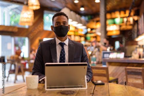 Businessman using laptop while wearing protective facial mask in coffee shop