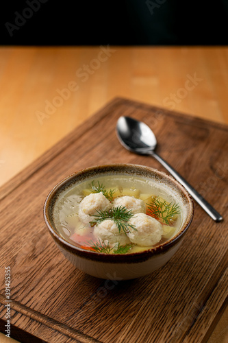 Russian meatball soup in.a small rustic bowl on a wooden table with a spoon aside