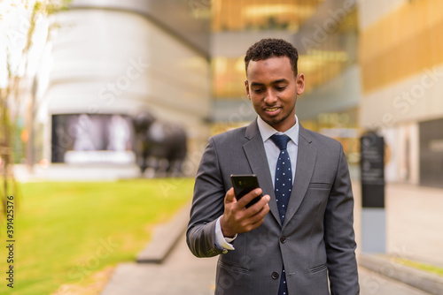 Happy African businessman outdoors smiling and using phone
