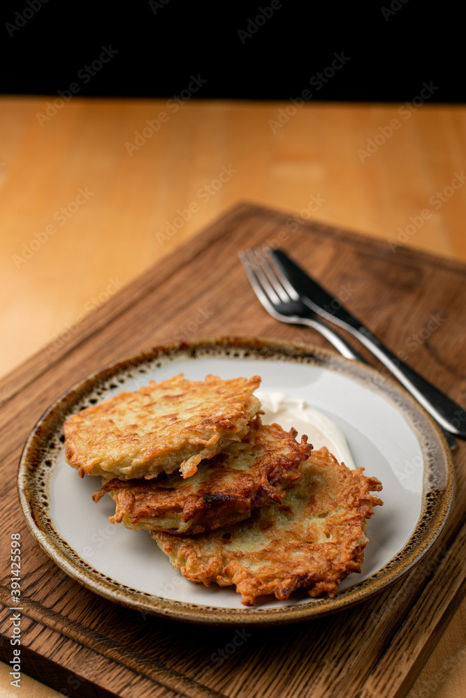 Crunchy and golden potato fritters ? rustic vegetarian snack with sour cream, appetising close up Crunchy and golden potato fritters ? rustic vegetarian snack with sour cream, appetising close up