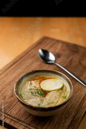 Chicken soup with boiled egg, cut in half and chicken breast pieces, small clay bowl, close up