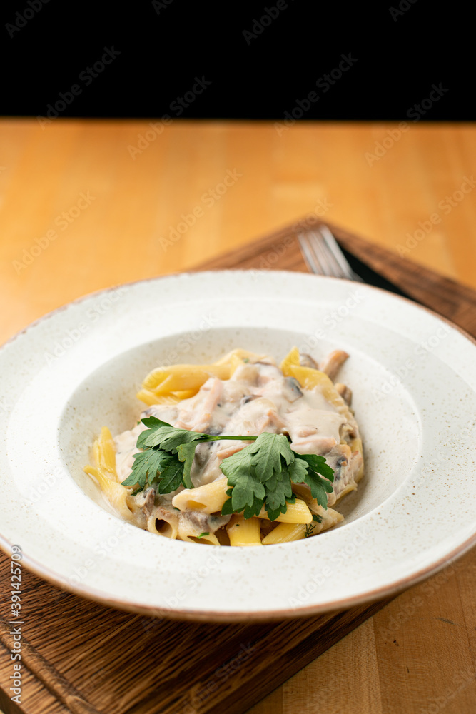 Chicken alfredo pasta with creamy sauce close up in a wide white dish on a wooden table
