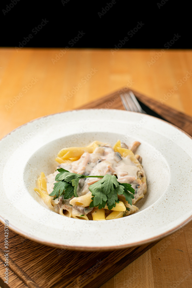 Chicken alfredo pasta with creamy sauce close up in a wide white dish on a wooden table Chicken alfredo pasta with creamy sauce close up in a wide white dish on a wooden table