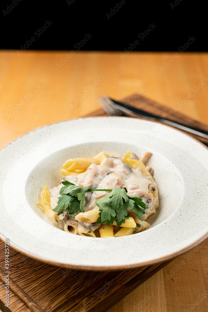 Chicken alfredo pasta with creamy sauce close up in a wide white dish on a wooden table Chicken alfredo pasta with creamy sauce close up in a wide white dish on a wooden table