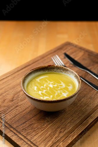 Bright yellow corn soup with cream swirls on wooden table, side view, close up in a studio, menu photo