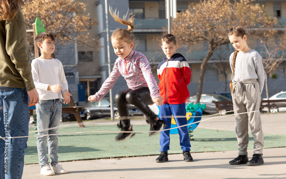 Fototapeta premium Happy smiling little friends playing with chinese jumping rope at playground. High quality photo
