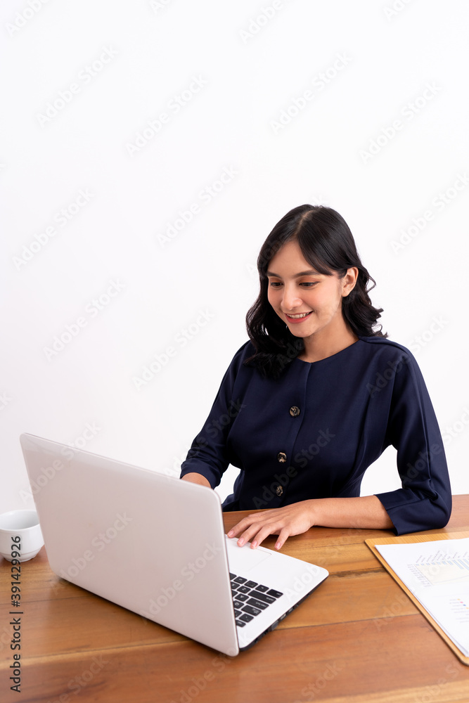 Attractive cheerful young business woman working on laptop and smiling while sitting. At her desk modern office Attractive cheerful young business woman working on laptop and smiling while sitting. At her desk modern office