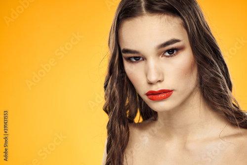 Beautiful brunette naked shoulders bright makeup red lips hairstyle close-up yellow background