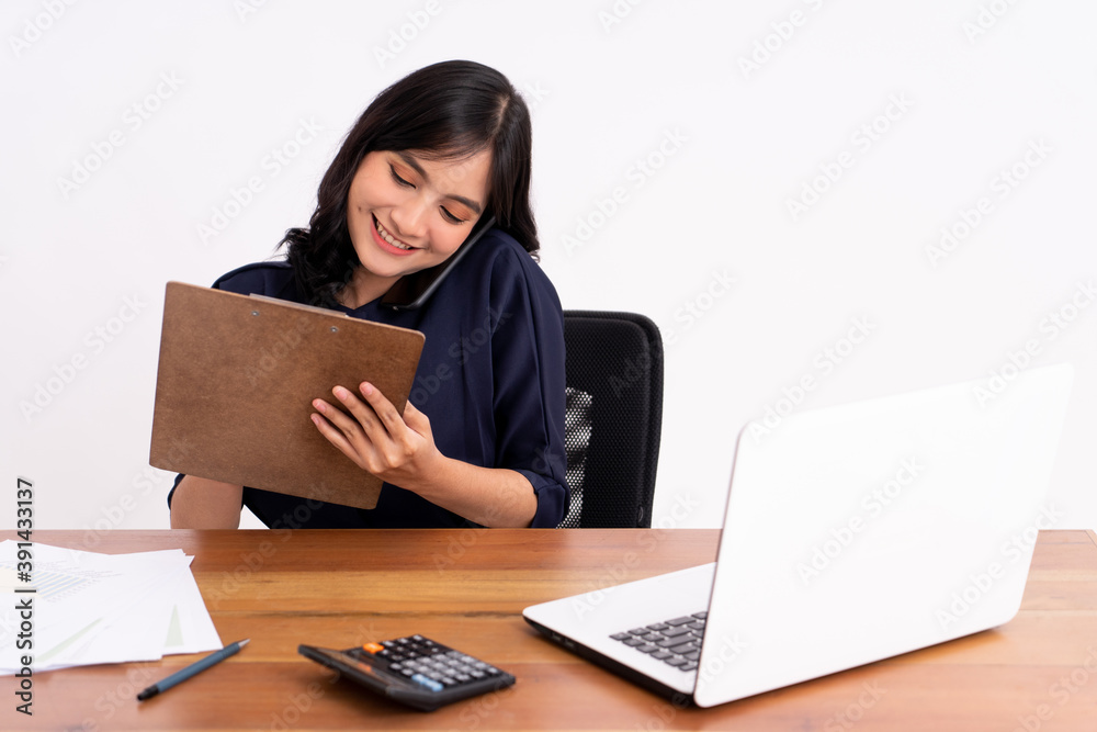 An attractive, busy and cheerful business woman holds a cell phone and smiles while sitting down. On modern office desk An attractive, busy and cheerful business woman holds a cell phone and smiles while sitting down. On modern office desk