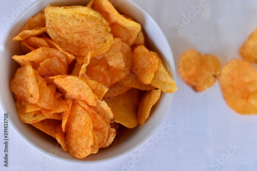 Close-up of potato chips or crisps in bowl against white background/ Unhealthy spicy snack