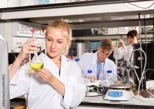 Young Caucasian female student viewing flask of liquor at chemical lab